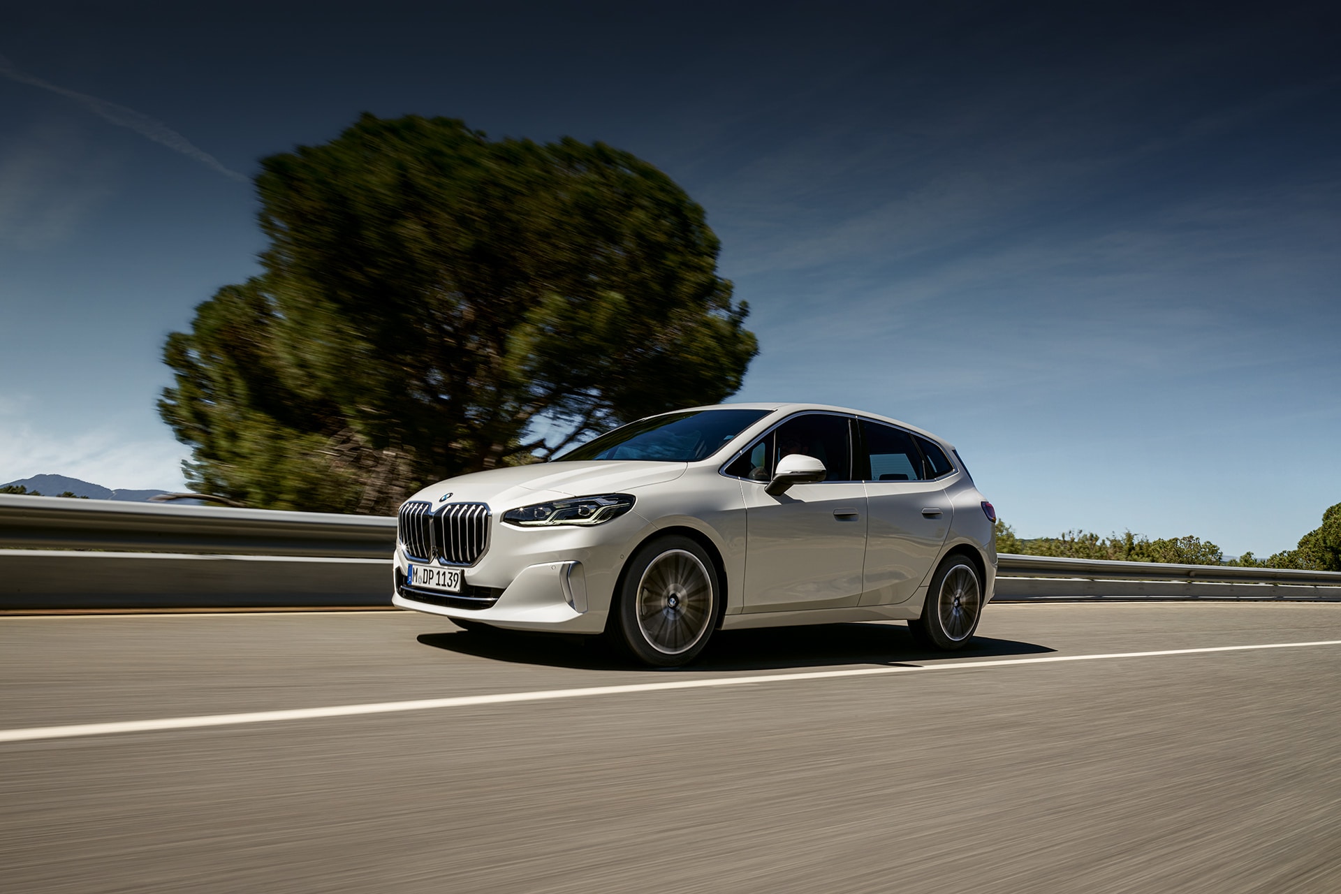 Weißer BMW 2er Active Tourer fährt auf Landstraße, klarer blauen Himmel und unscharfer Hintergrund