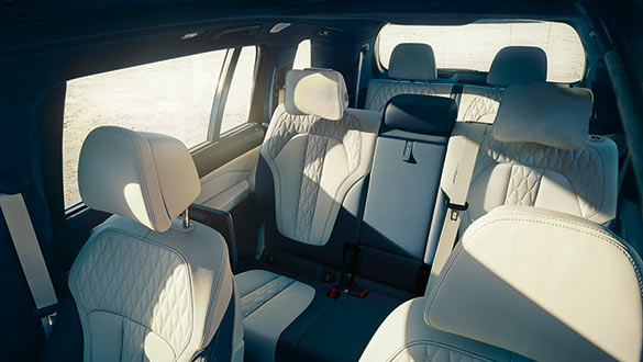 Interieur des luxuriösen BMW X7 mit weißem Leder, Panoramadach und stilvoller Holzverkleidung mit Blick auf bergige Landschaft.