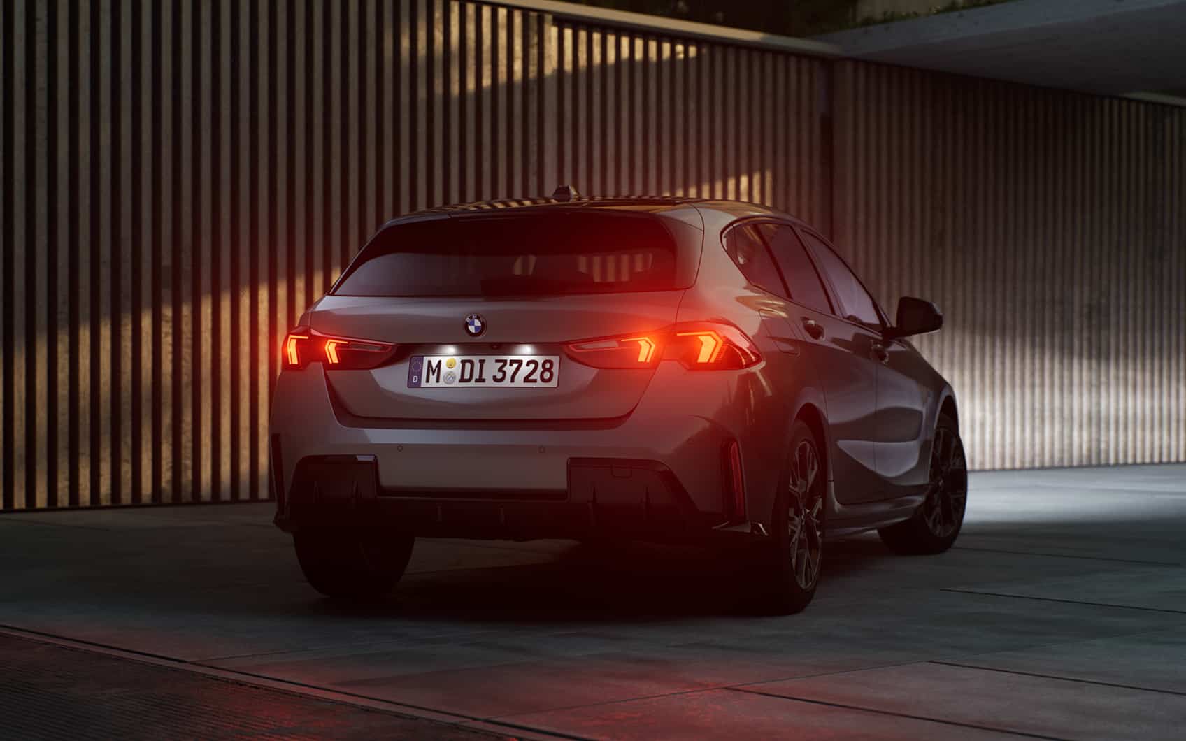 Grauer BMW 1er in der Dämmerung. Die roten Hecklichter strahlen.