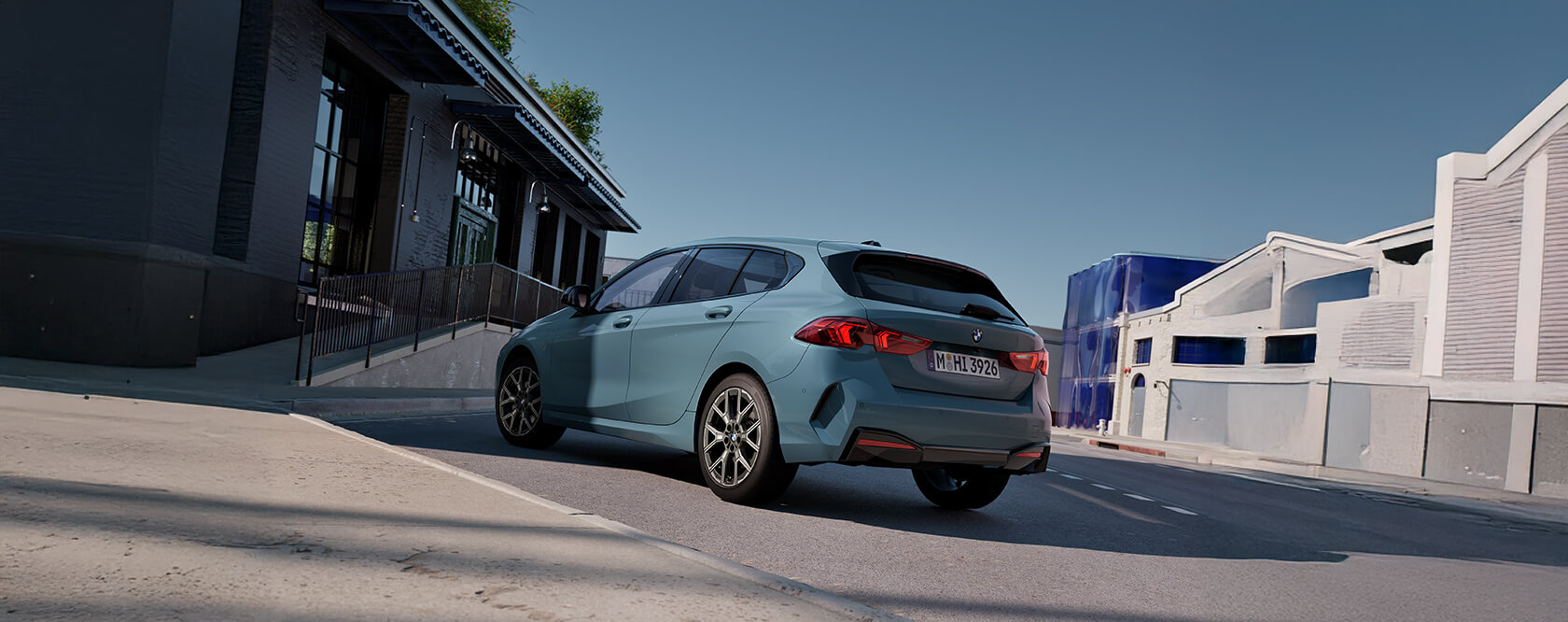 Heckansicht eines blauen BMW 1er auf einer Straße vor modernen Gebäuden bei Tageslicht.