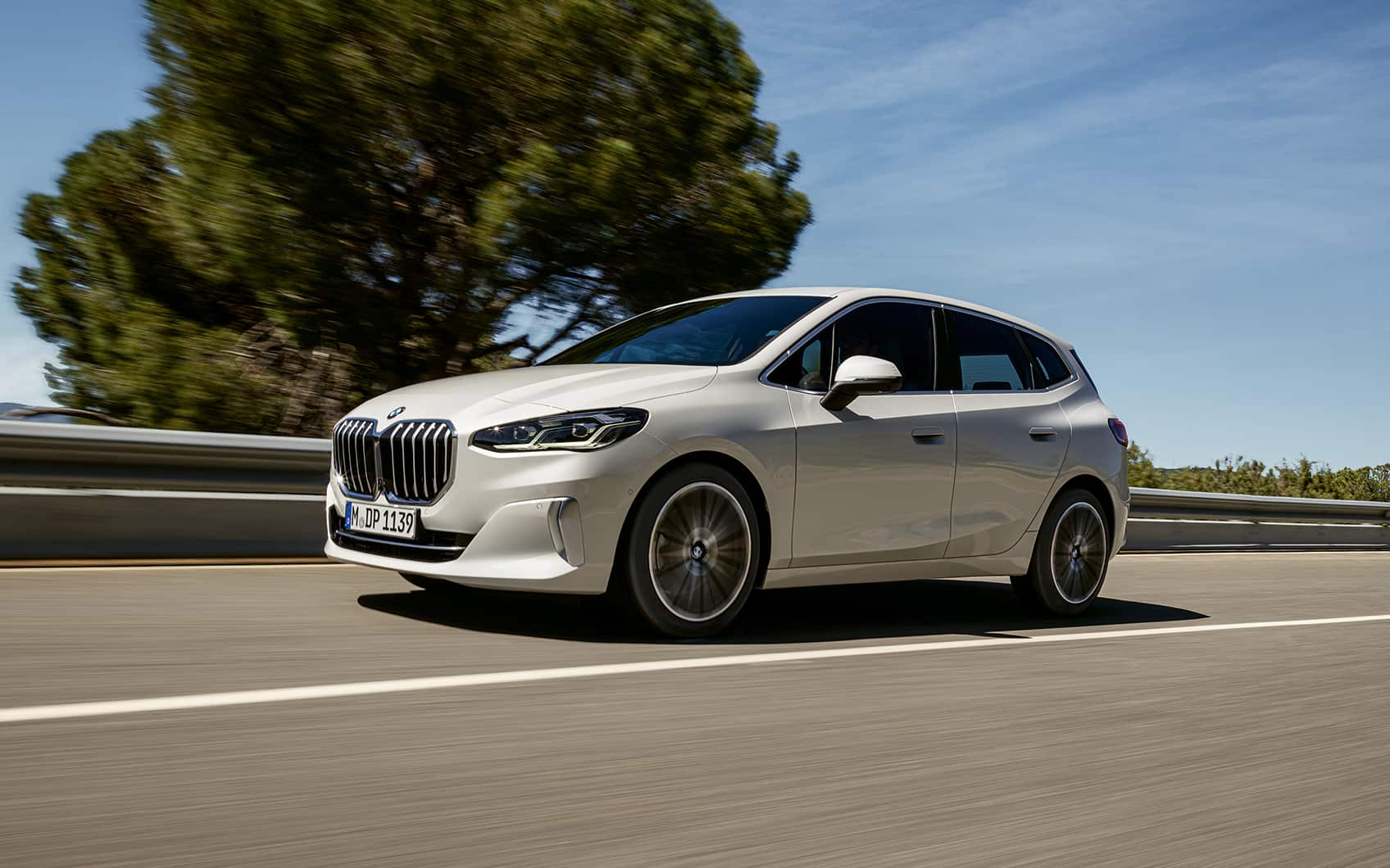 Weißer BMW 2er Active Tourer fährt auf Landstraße, klarer blauen Himmel und unscharfer Hintergrund