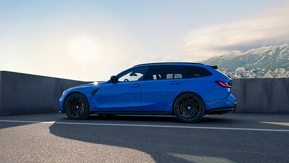 Seitenansicht eines blauen BMW 3er Competition Touring M Automobils auf einem Parkhausdach, Berglandschaft im Hintergrund