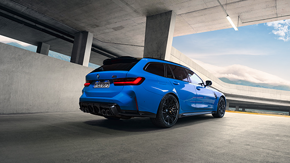 Heckansicht auf ein blaues BMW 3er Competition Touring M Automobil in einem futuristischen Parkhaus mit Blick auf eine Berglandschaft im Hintergrund