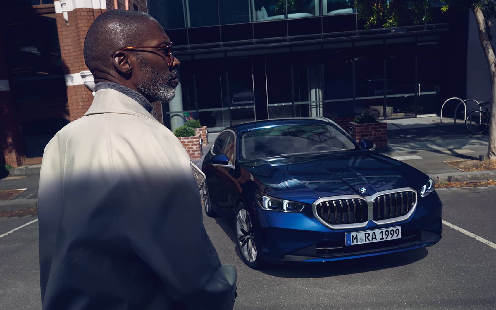 Dunkelblaue BMW 5er Limousine parkt in urbaner Szene, stilvoll gekleideter Mann schaut darauf