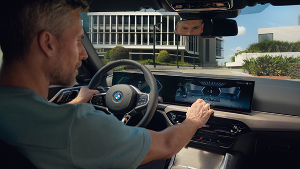 Blick über die Schulter eines Mannes mittleren Alters auf dem Fahrersitz eines BMW i4, der das Display bedient