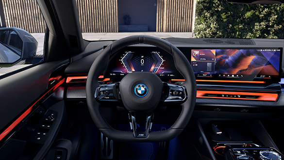 BMW i5 Fahrerplatz mit multifunktionalem Lenkrad und BMW Curved Display, orangene Akzente