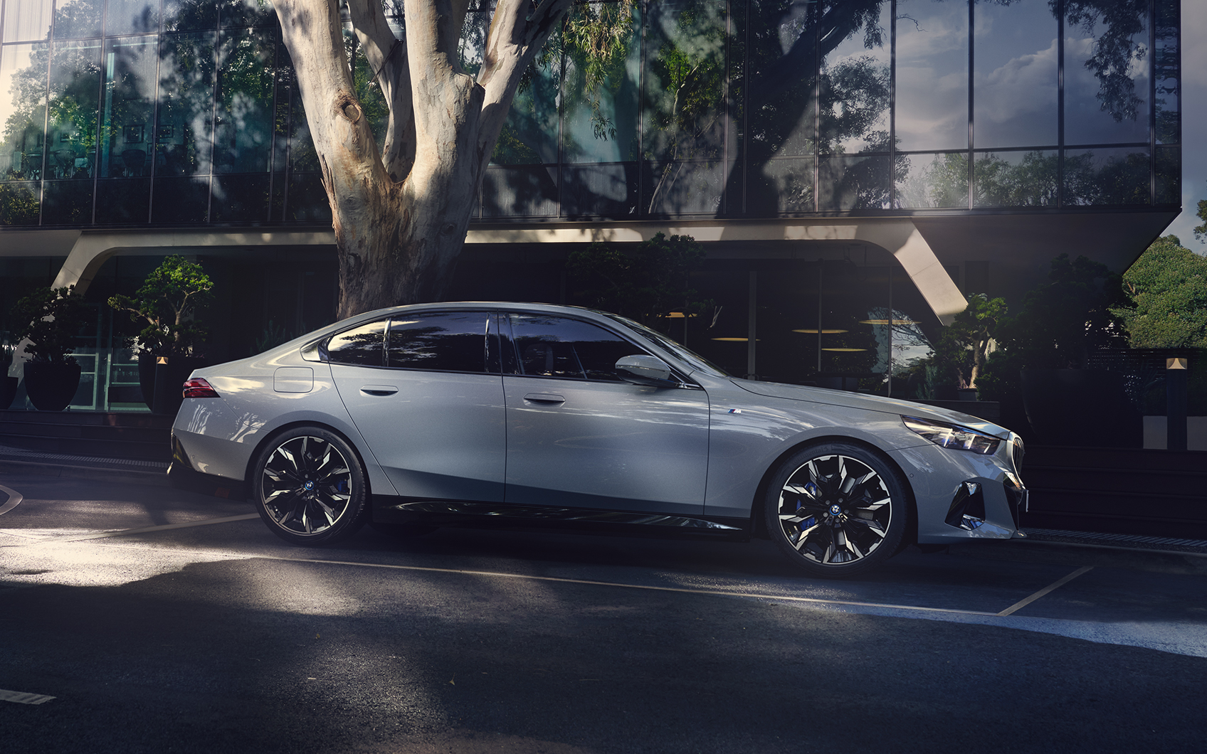 Silberner BMW i5 geparkt in urbaner Szenerie mit verglastem Bürogebäude und Bäumen