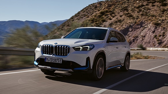 Elektrischer BMW iX1 fährt tagsüber auf einer Straße umgeben von Bergen