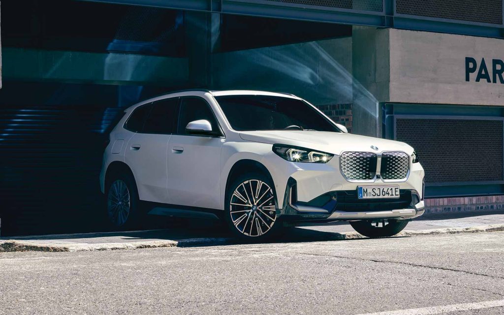 Weißer BMW iX1 kommt aus einer Ausfahrt auf die Straße gebogen.