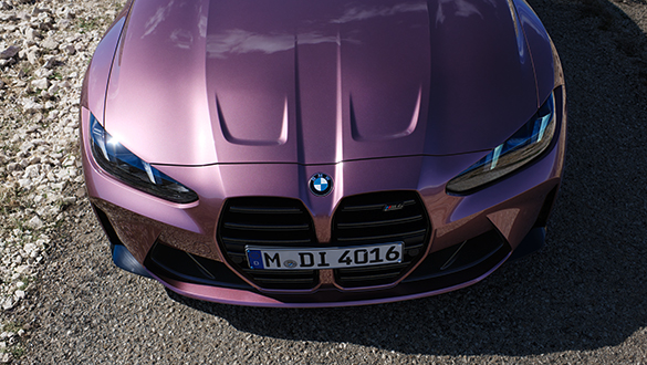 Vogelperspektive auf die Motorhaube eines rosanen BMW M4 Competition Cabrios, Fokus auf die Scheinwerfer und das BMW Emblem