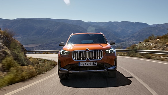 BMW X1 fährt auf sonniger Landstraße, blauer Himmel und verschwommenen Bergen im Hintergrund