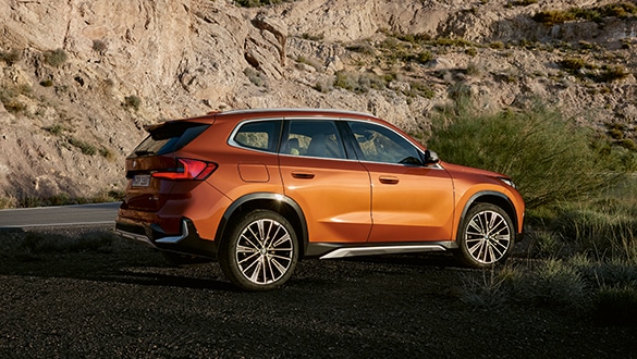 BMW X1 in Orange in felsiger Landschaft, hintere Seitansicht, sonniges Wetter