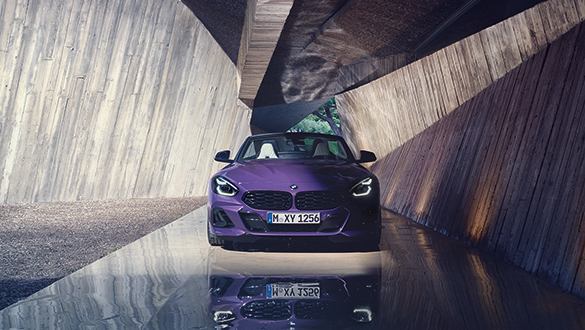 Lila BMW Z4 Roadster mit Metallic-Lackierung unter Betonbrücke, Reflexion auf nasser Oberfläche, Betrachterblick auf Frontdesign.