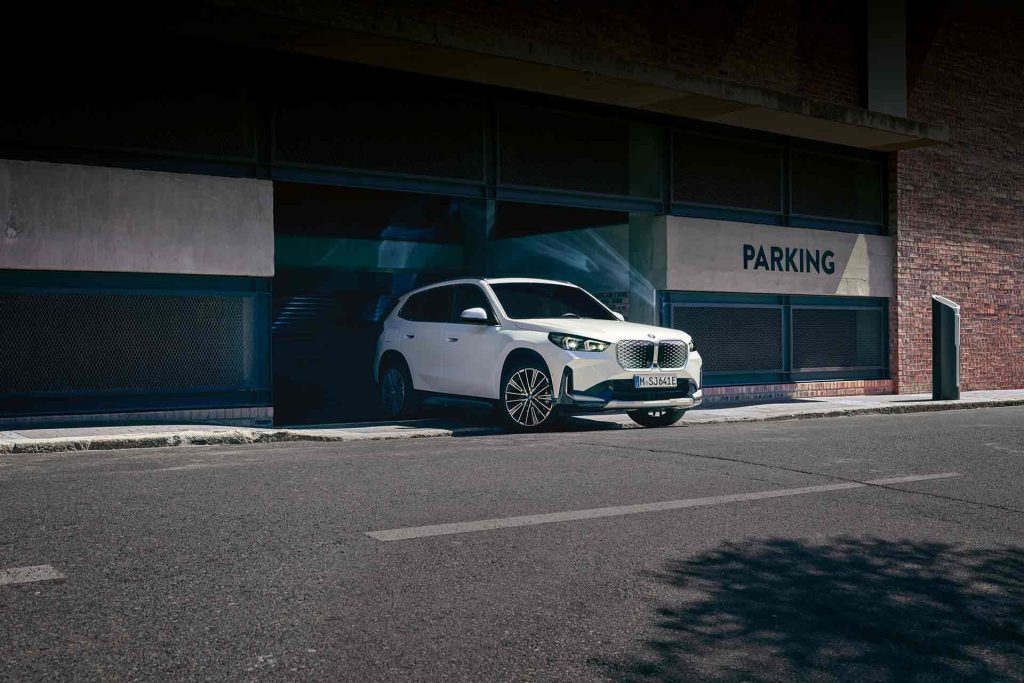 Weißer BMW iX1 kommt aus einer Ausfahrt auf die Straße gebogen.