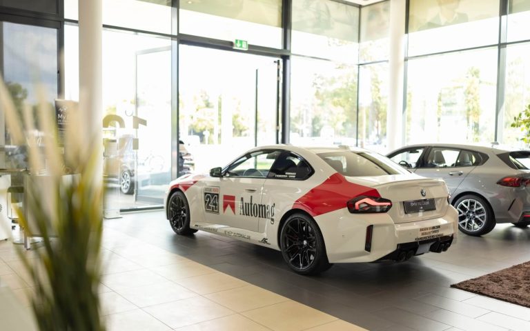 Seitenansicht der linken Seite eines BMW M2 Coupé in Malboro Optik mit Fokus auf die linke Heckleuchte, den Vorder- und Hinterreifen und den Automag Schriftzug im Malboro Design im Showroom der Automag