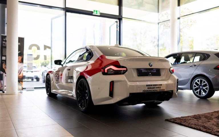 Heckansicht eines BMW M2 Coupé in Malboro Design mit Fokus auf die linke Heckleuchte und den linken Hinterreifen im Showroom der Automag