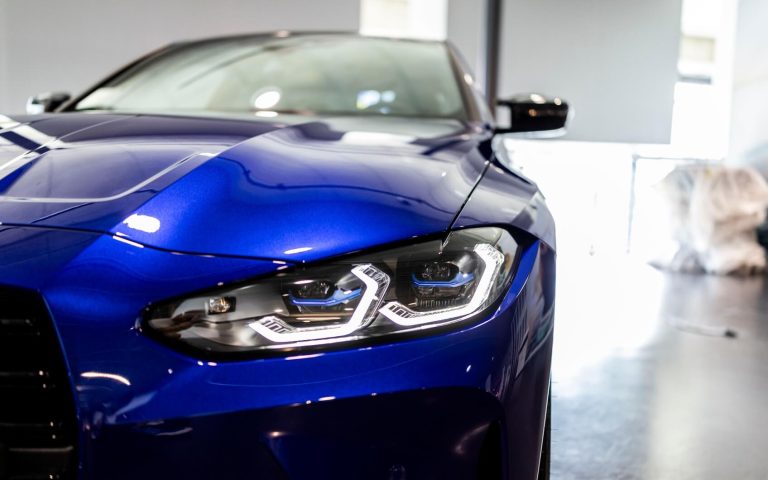 Detailaufnahme des linken Frontscheinwerfers eines BMW M4 Competition Coupé, getunt von AC Schnitzer, in der Farbe Dunkelblau, aufgenommen im Showroom der Automag