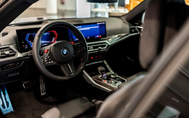 Cockpit eines BMW M4 Competition Coupé, getunt von AC Schnitzer, fotografiert durch die geöffnete Fahrertür mit Fokus auf das BMW M Lenkrad und die Bedienelemente im Showroom der Automag