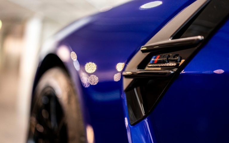 Detailaufnahme des M4 Schriftzuges auf einem BMW M4 Competition Coupé in der Farbe Dunkelblau, getunt von AC Schnitzer, aufgenommen im Showroom der Automag