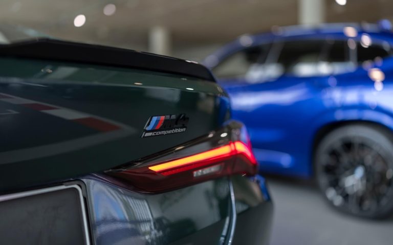 Detailaufnahme der rechten Heckleuchte eines BMW M4 Competition Coupé in der Farbe Grün mit Fokus auf den M4 Competition Schriftzug über der Heckleuchte, aufgenommen im Showroom der Automag