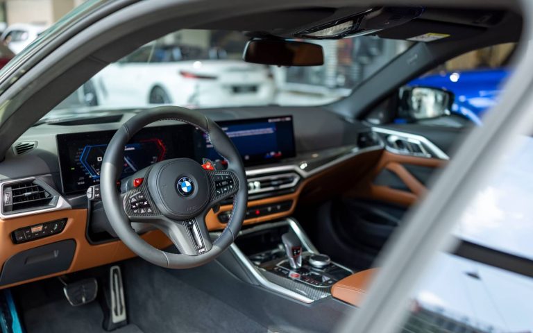 Cockpit eines BMW M4 Competition Coupé, fotografiert durch die geöffnete Fahrertür mit Fokus auf das BMW Lenkrad und braune Interieurleisten, aufgenommen im Showroom der Automag