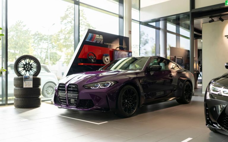 Frontaufnahme eines BMW M4 Competition Coupé in der Farbe Violett mit Fokus auf die linke Seite es Fahrzeuges, aufgenommen im Showroom der Automag