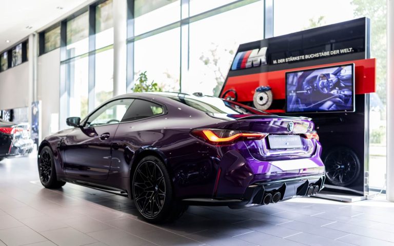 Heckaufnahme eines BMW M4 Competition Coupé in der Farbe Violett, im Fokus steht die linke Seite des Fahrzeugs, aufgenommen im Showroom der Automag