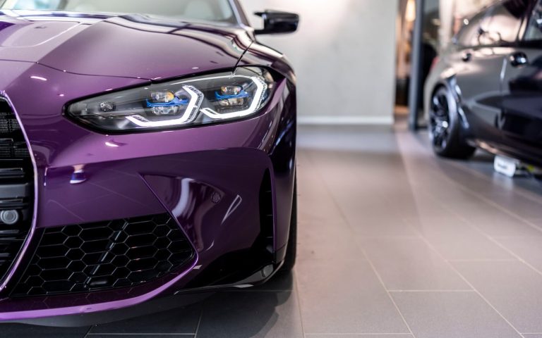 Detailaufnahme des linken Frontscheinwerfers eines BMW M4 Competition Coupé in der Farbe Violett, aufgenommen im Showroom der Automag