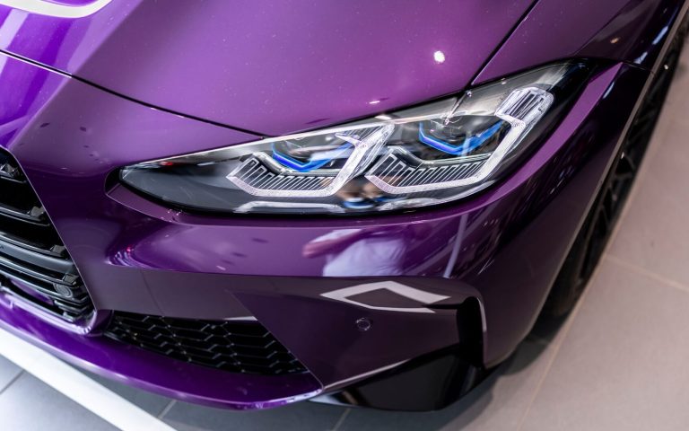 Vogelperspektive auf den linken Frontscheinwerfer eines BMW M4 Competition Coupé in der Farbe Violett, aufgenommen im Showroom der Automag