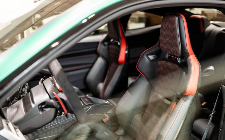 Interieur des vorderen Bereichs eines BMW M4 Coupé mit Fokus auf den Fahrer- und Beifahrersitz in den Farben Schwarz und Rot, aufgenommen durch die geöffnete Fahrertür im Showroom der Automag