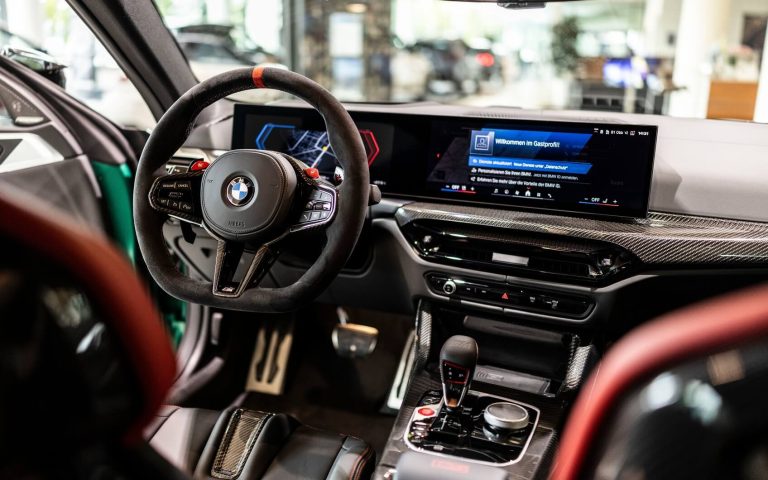 Cockpit des BMW M4 Coupé mit Fokus auf das BMW M Lederlenkrad und das Display, aufgenommen von der Rückbank im Showroom der Automag