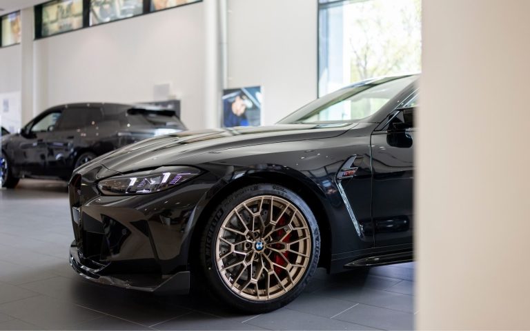 Seitenansicht eines BMW M4 Coupé in der Farbe Schwarz mit Fokus auf die linke Front mit dem Scheinwerfer und den Vorderreifen, aufgenommen im Showroom der Automag