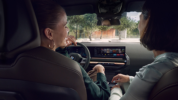 Innenaufnahme eines BMW X3 M Automobil aus Sicht des Rückfahrers mit Fokus auf die Fahrerin, Beifahrerin und das Cockpit mit dem Lederlenkrad, den Bedienelementen und das BMW Curved Display