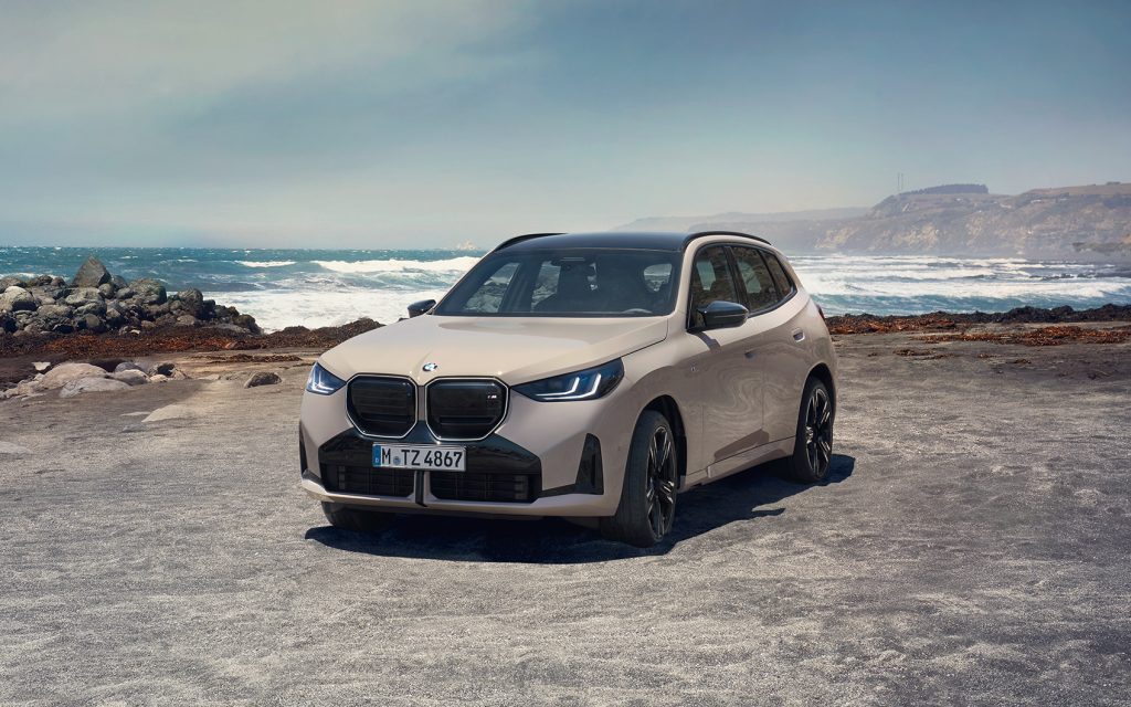 Grauer BMW X3 M Automobil geparkt an einer Küste mit Meer im Hintergrund