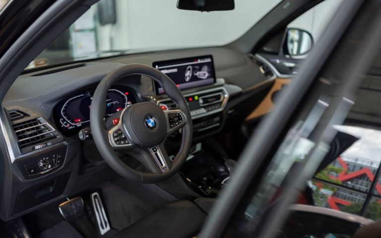 Cockpit eines BMW X3 M Competition mit Fokus auf das BMW Lederlenkrad und die Bedienelemente, aufgenommen durch die geöffnete Fahrertür im Showroom der Automag