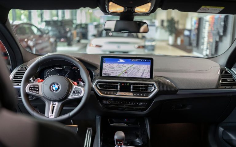 Cockpit des BMW X4 M Competition mit Fokus auf das Display und das BMW Lederlenkrad, aufgenommen von der Rückbank im Showroom der Automag