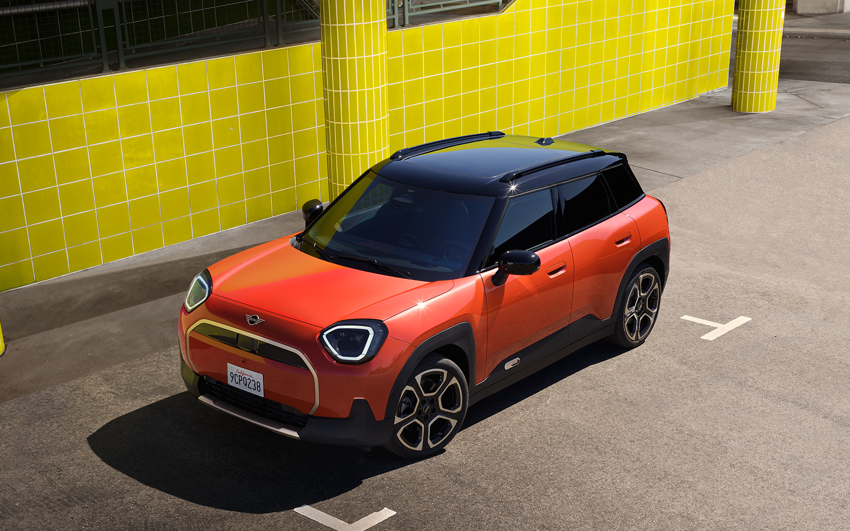 Vogelperspektive auf einen orangenen MINI Aceman, geparkt vor einer gelben Wand in einem Parkhaus