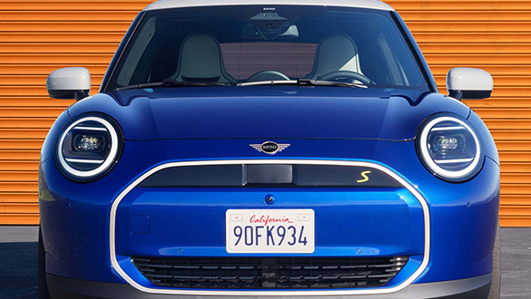 Blauer MINI Cooper Electric mit kalifornischem Kennzeichen vor warmer, texturierter Wand