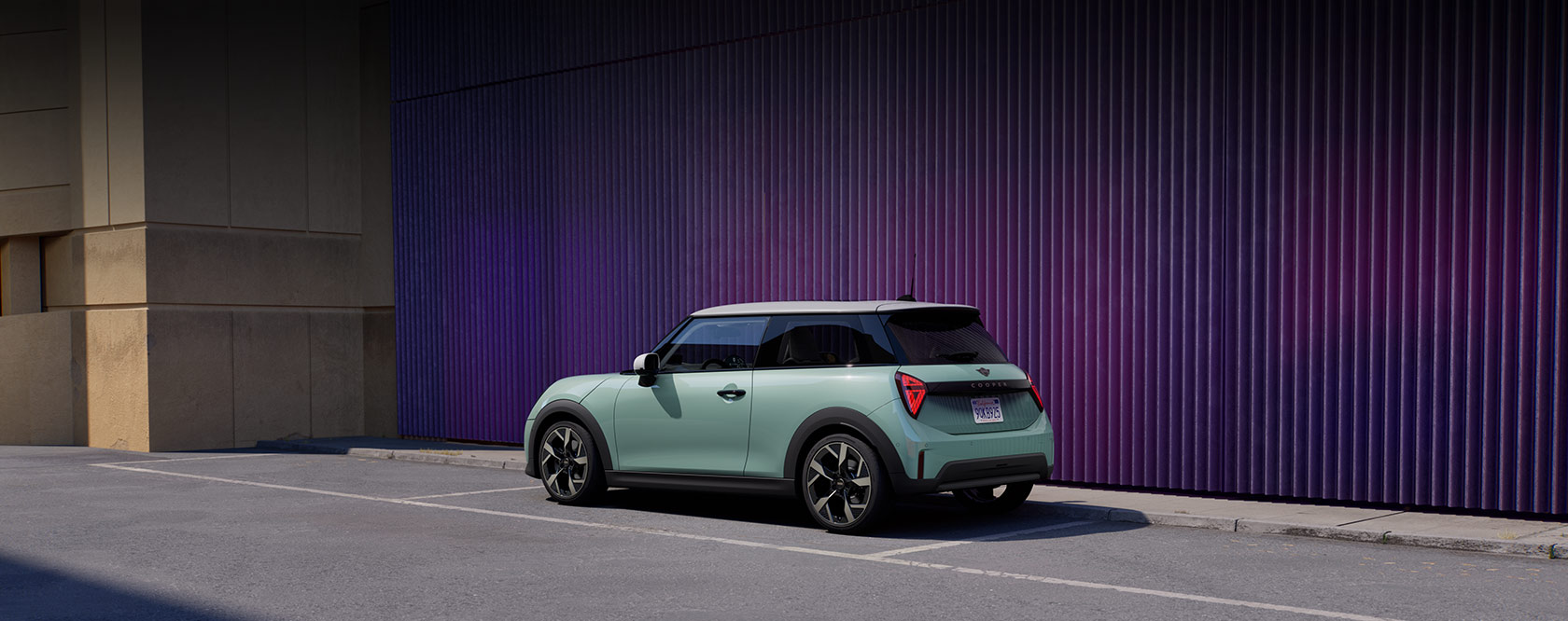 Mintgrüner Mini Cooper mit weißem Dach auf einem Parkplatz vor lila Wand