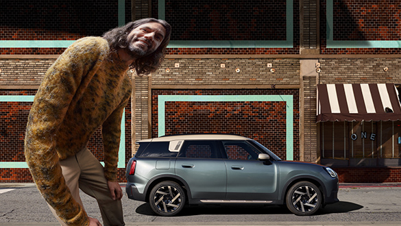 MINI Countryman in mattem Grau mit grünstich, sportlichen Felgen und robustem Design, geparkt an städtischer Straßenecke mit spielerischer Kulisse.