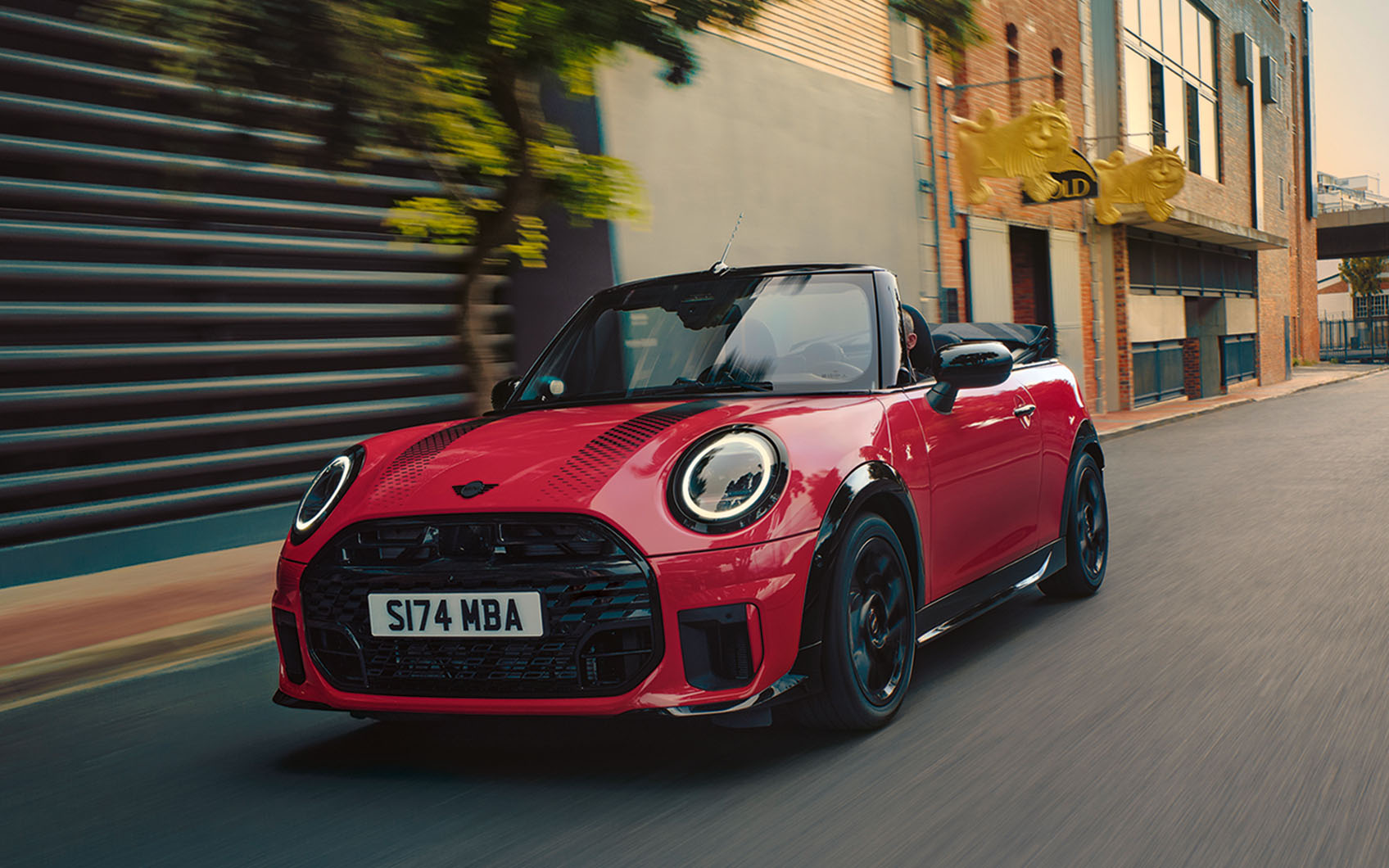 Roter Mini Cabrio fährt durch eine urbane Straße bei Tageslicht.
