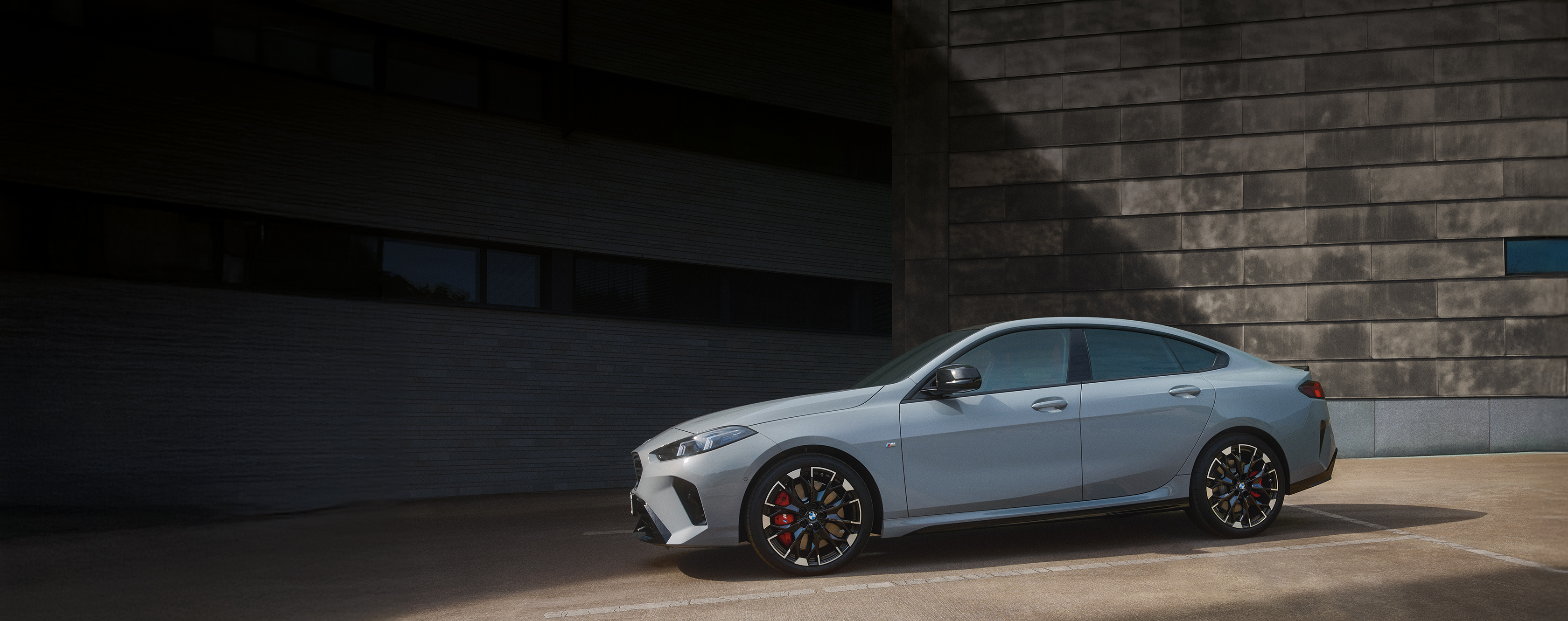 Seitenansicht eines parkenden BMW 2er Gran Coupé in der Farbe Grau mit roter M Sportbremse vor dunkler Wand