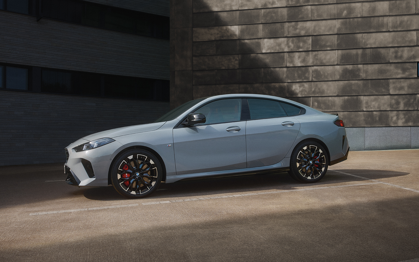 Seitenansicht eines parkenden BMW 2er Gran Coupé in der Farbe Grau mit roter M Sportbremse vor dunkler Wand