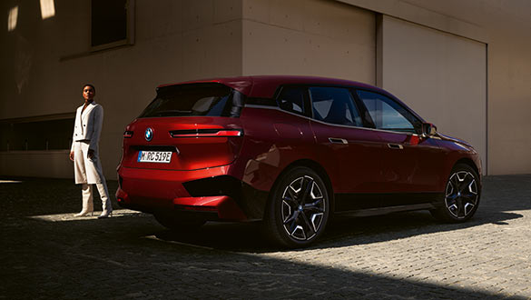 Roter BMW iX von der Seite, parkt vor minimalistischem Gebäude, neben stilvoller Person