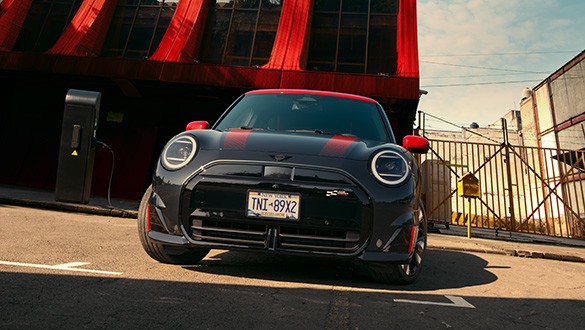 Frontansicht eines parkenden MINI John Cooper Works Electric in der Farbe Schwarz mit roten Sport Stripes und JCW Bodykit, Frontschürze in Hochglanzschwarz