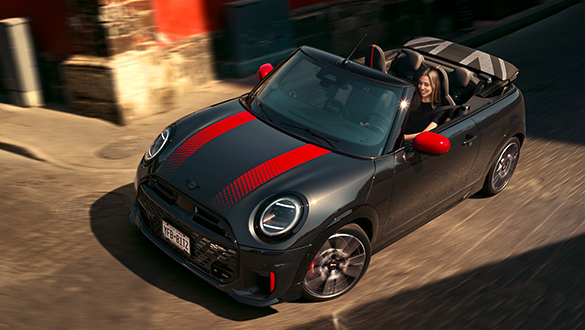 Blick von oben auf ein MINI John Cooper Works Cabrio in der Farbe Schwarz mit roten Sport Stripes und geöffnetem Dach in Fahrt