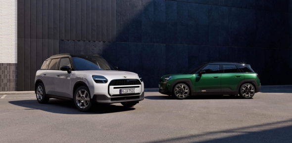 Frontansicht eines weißem MINI Aceman und Seitenansicht eines grünen MINI Countryman, geparkt vor einem Gebäude