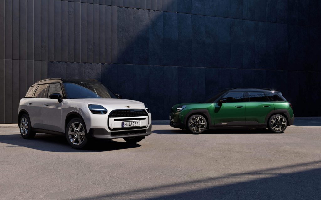 Frontansicht eines weißem MINI Aceman und Seitenansicht eines grünen MINI Countryman, geparkt vor einem Gebäude