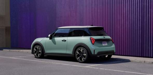 Mintgrüner Mini Cooper mit weißem Dach auf einem Parkplatz vor lila Wand