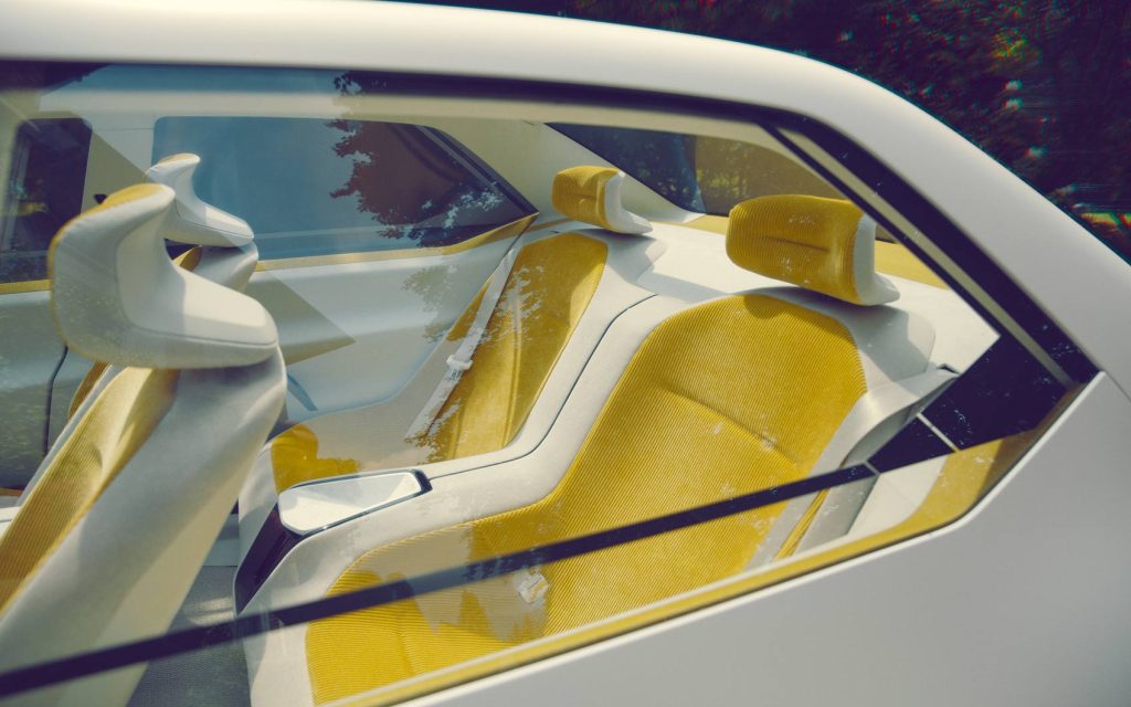 Blick durch die Seitenscheibe auf gelbe Rücksitze eines modernen Elektroautos mit minimalistischer Innenausstattung.